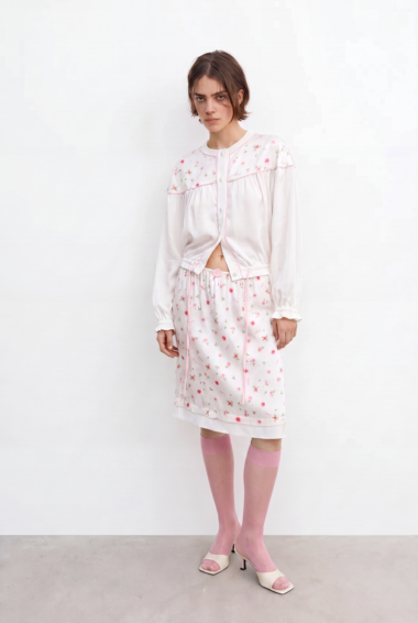 Woman in a pale pink floral pajama set with a matching cardigan, pink knee-high socks, and beige heeled sandals against a white backdrop.