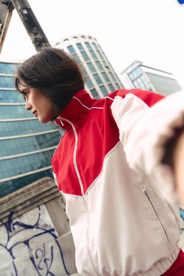 Person in a red and white jacket leaning against a graffiti-covered wall with modern glass buildings in the background, city street vibe.