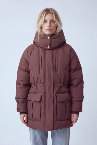 Woman in a oversized brown puffer coat with a high collar and large front pockets, posing against a light backdrop.