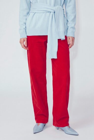Person wearing a light blue knit sweater with a sash belt, red corduroy trousers, and light blue pointed-toe flats.